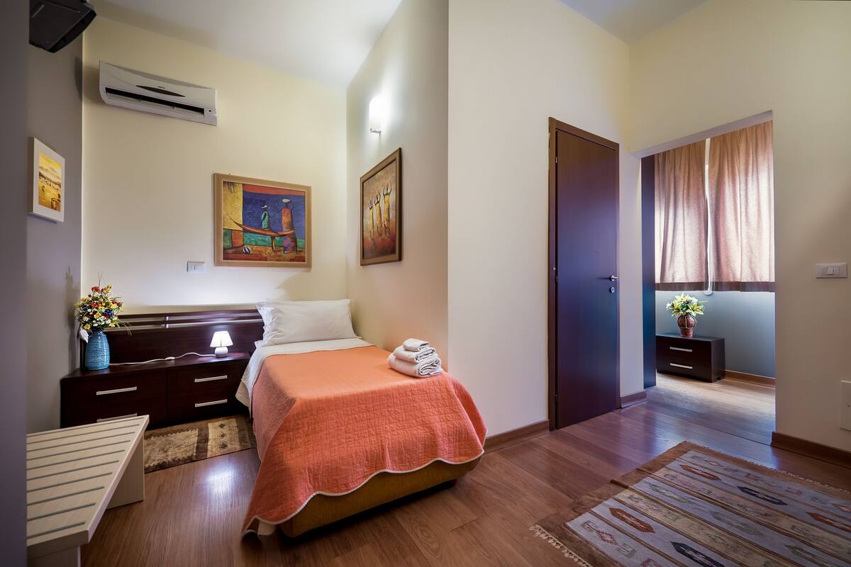A bedroom with a bed, nightstand, dresser, and a window with curtains.
