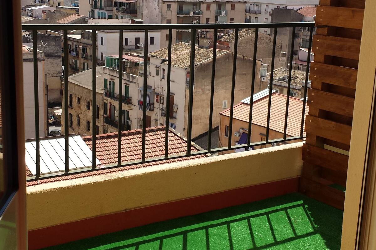 A balcony with a view of a cityscape, a green artificial turf floor, and a wooden railing.