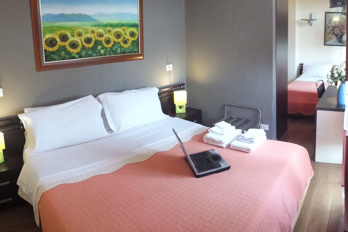 A hotel room with a bed, a laptop, and a bedside table with a lamp.