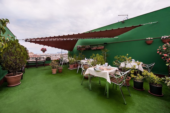 Une terrasse sur le toit, aménagée avec des tables et des chaises, entourée de plantes en pot et d’un mur végétal.