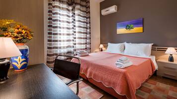 A hotel room with a bed, a desk, a chair, a lamp, a vase with flowers, and a painting on the wall.