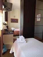 Una camera d'albergo con un letto, una scrivania con una lampada, una sedia, un tavolino e un quadro appeso al muro.