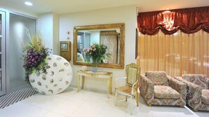 A living room with a large mirror, a round table with a vase of flowers, and patterned armchairs. - Hotel Cecere (Mottola)