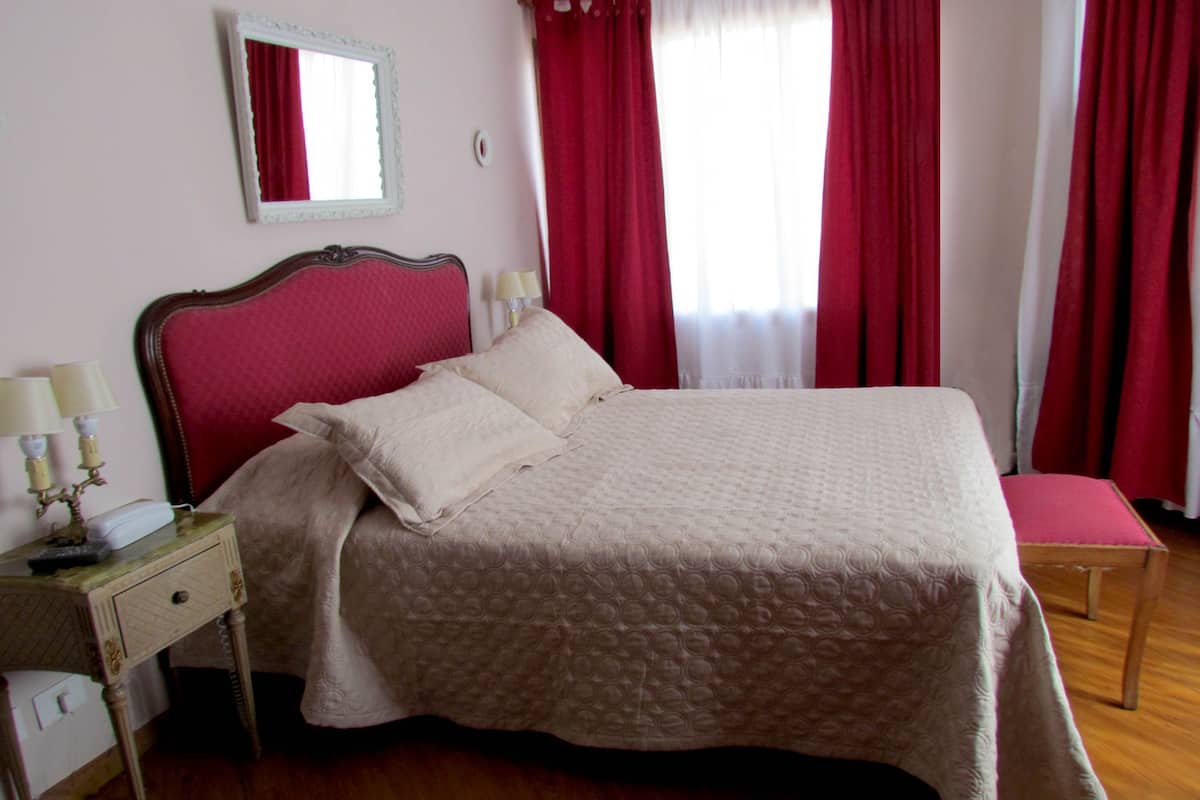 Una cama bien hecha con cabecera, una mesita de noche con lámpara y un espejo en la pared.