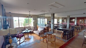 A spacious dining area with high ceilings, large windows, and a mix of seating arrangements including tables and chairs. - Hostería Meulen (El Calafate)