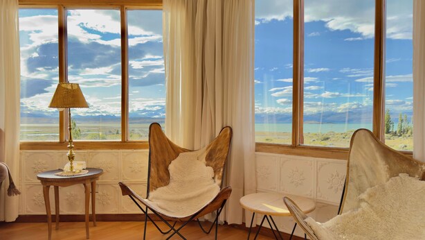 A room with large windows, a wooden floor, and two chairs with white cushions. - Hostería Meulen (El Calafate)