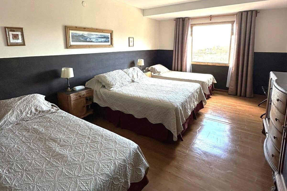 Habitación de hotel con dos camas, un aparador y una ventana con cortinas.