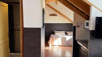 Ein kleines Zimmer mit Bett, Küchenzeile und Holzboden.