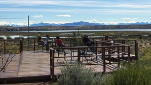 A wooden deck with metal chairs and tables overlooking a lake and mountains. - Hostería Meulen (El Calafate)