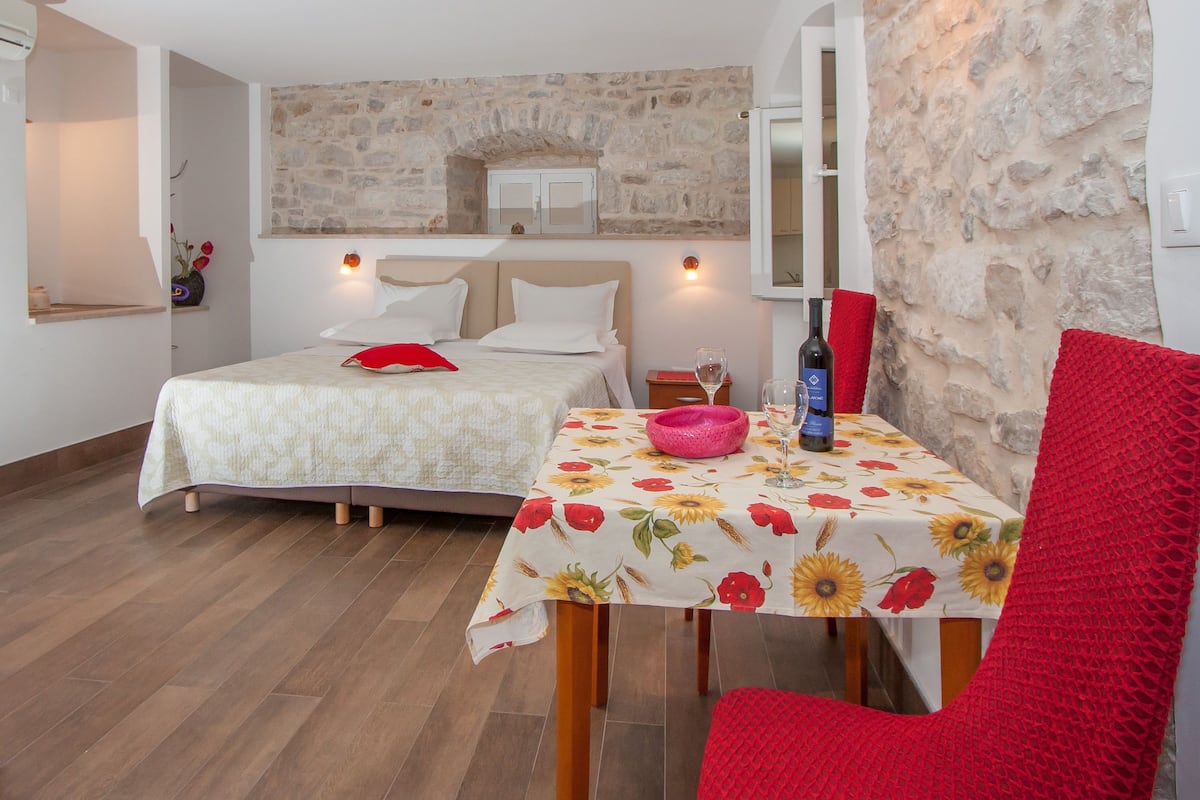 A bedroom with a bed, a table with a floral tablecloth, and a red chair.