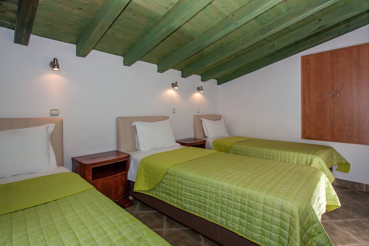 A room with three beds, wooden headboards, and a wooden wardrobe.