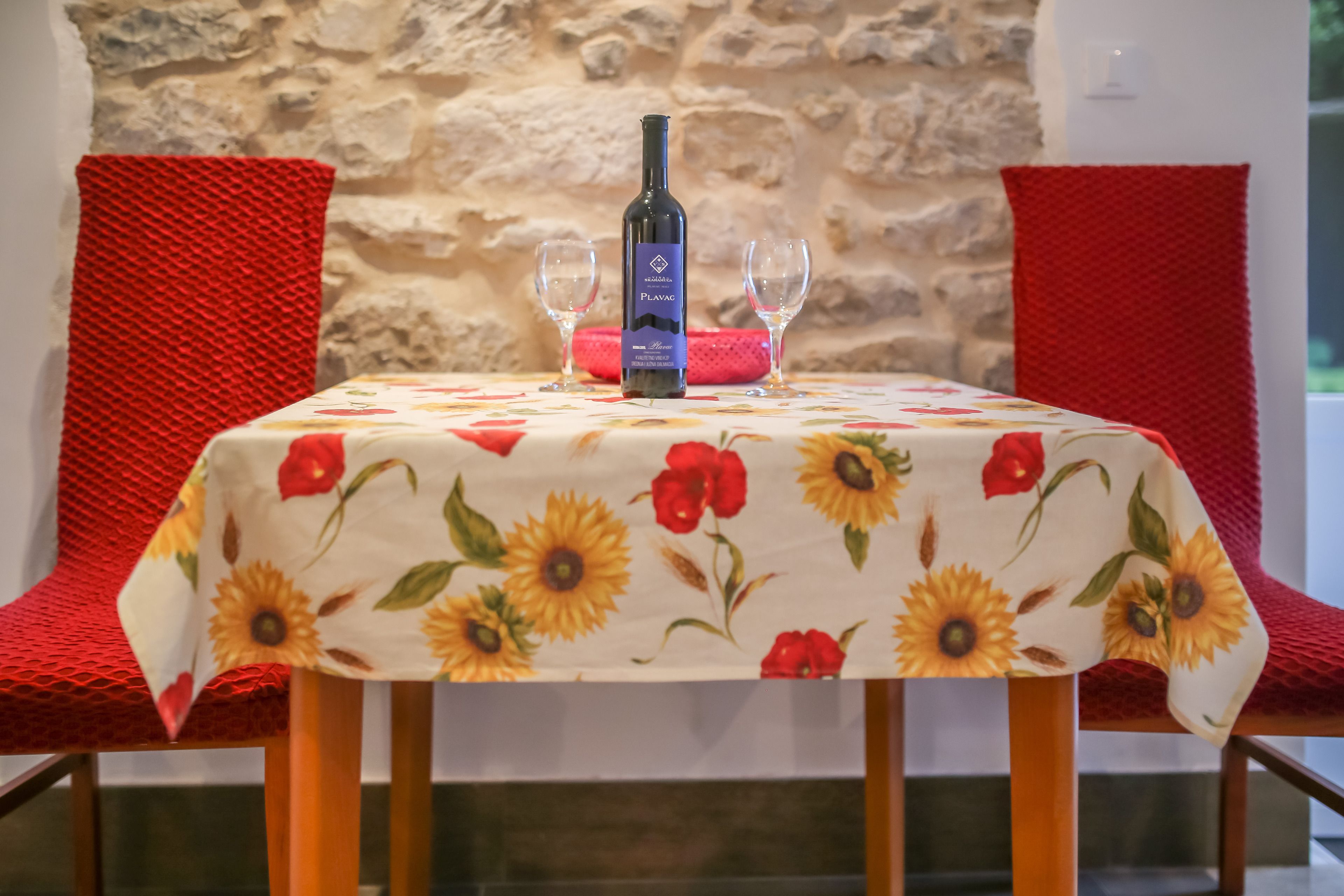 A table with a floral tablecloth, a bottle of wine, and two glasses.