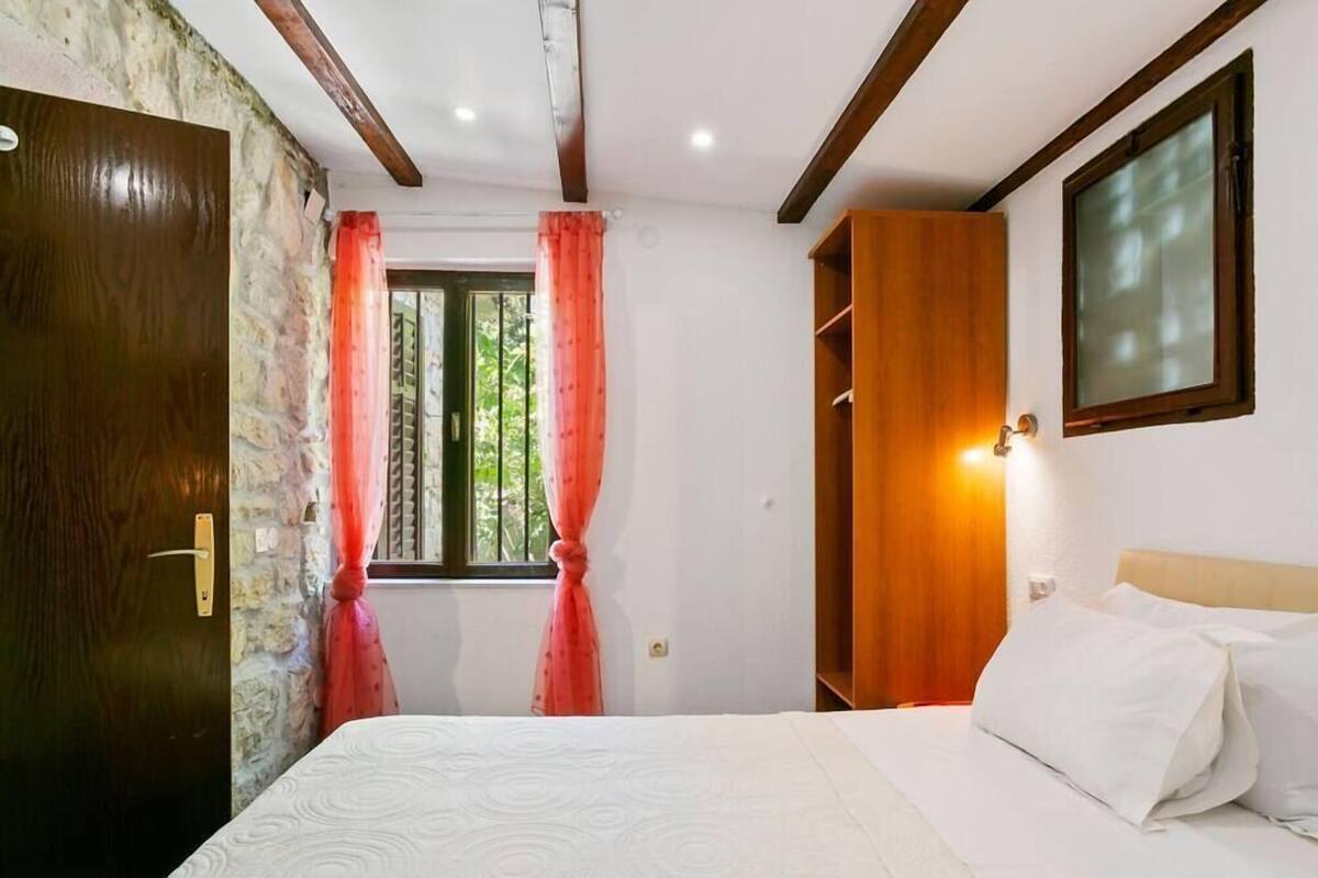 A bedroom with a bed, a wooden wardrobe, a window with curtains, and a wall-mounted light.