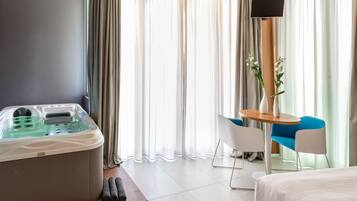 A hotel room with a large bathtub, a small table with two chairs, and a TV mounted on the wall.
