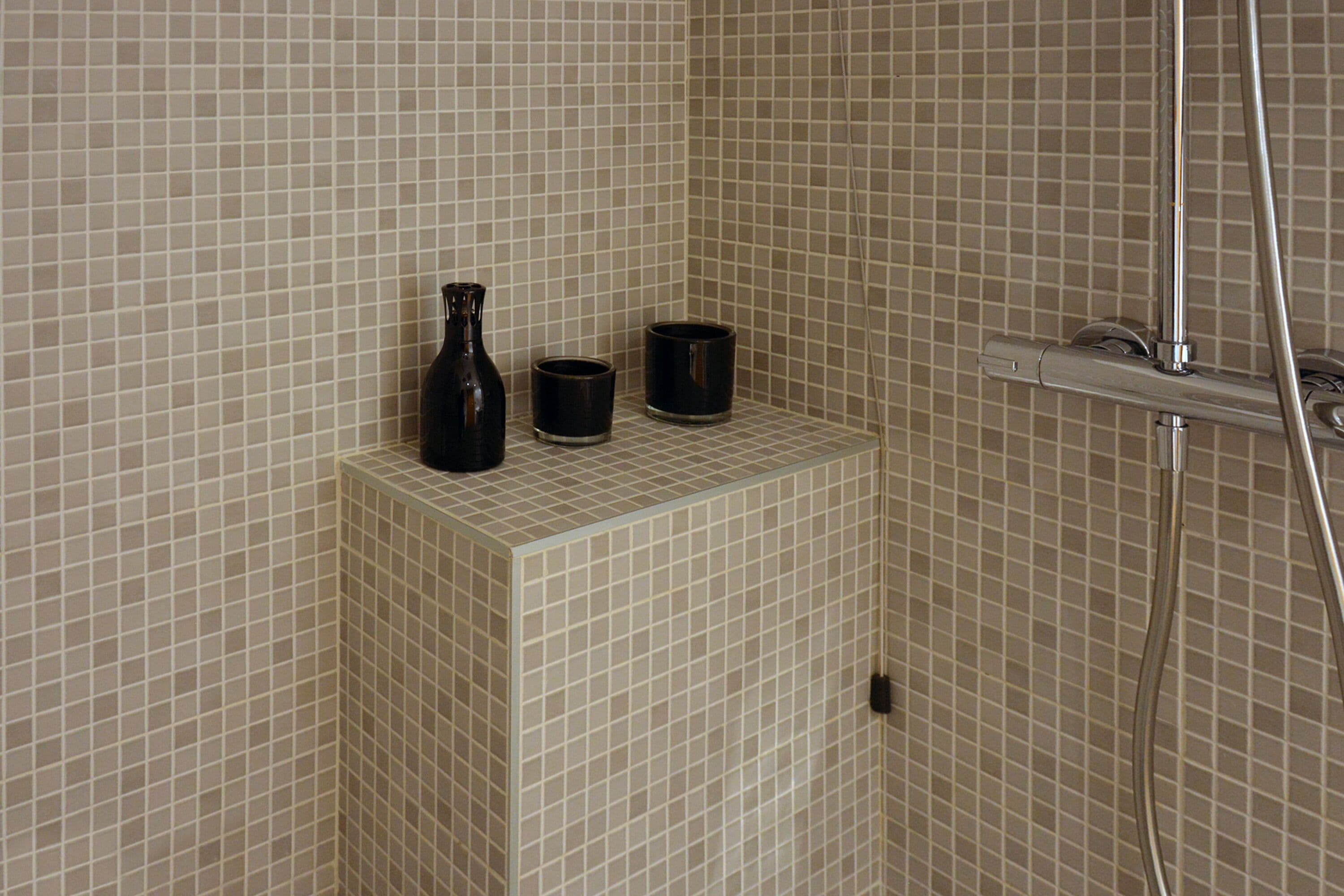 Un área de ducha con azulejos y un estante pequeño que sostiene un florero y dos tazas.
