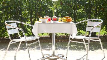 A table with a white tablecloth, two metal chairs, and a vase with flowers.