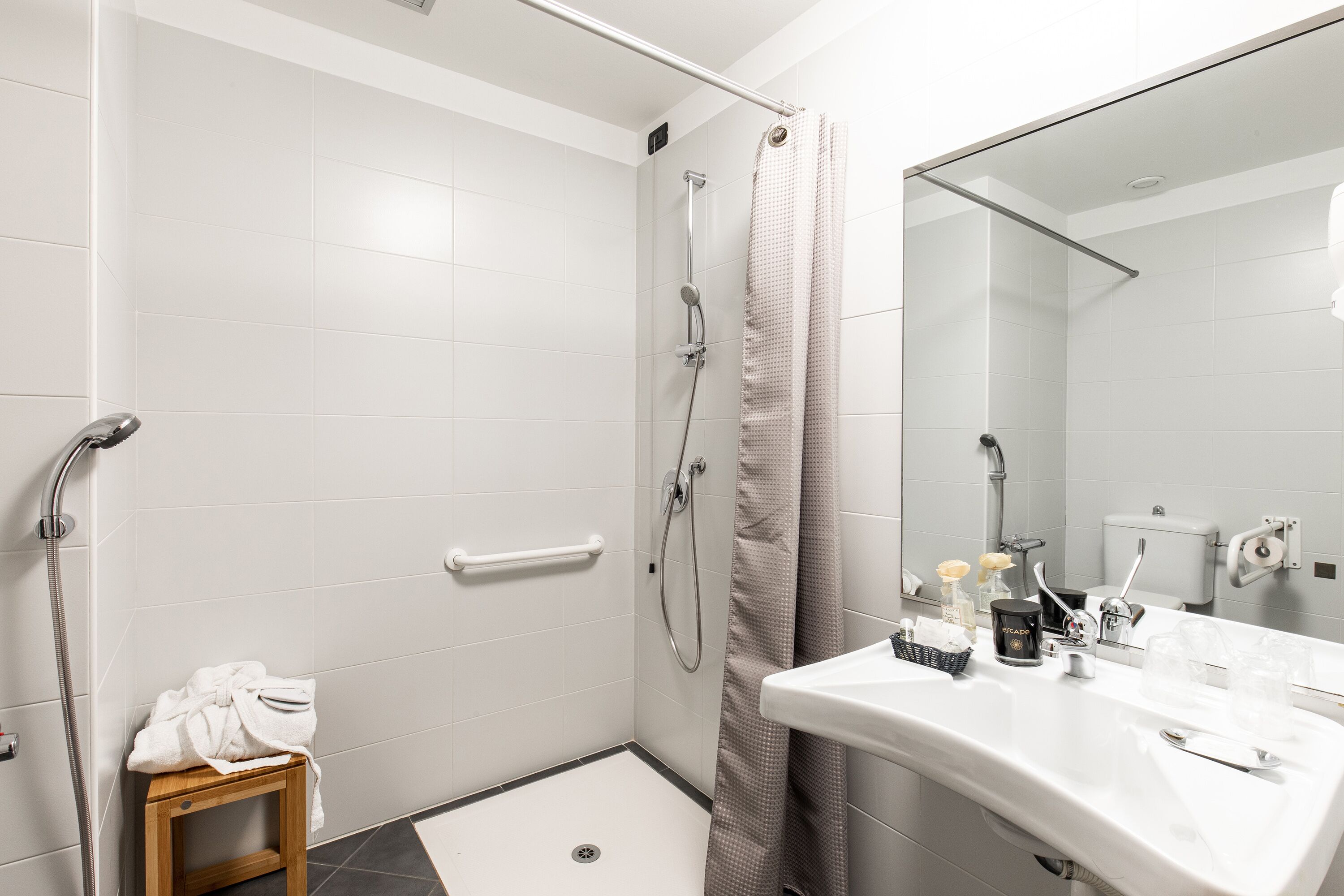 A modern bathroom with a shower, a sink with toiletries, and a small wooden stool.