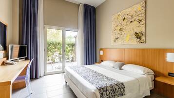 Habitación de hotel con cama, escritorio con computadora, televisor y un amplio ventanal con cortinas.