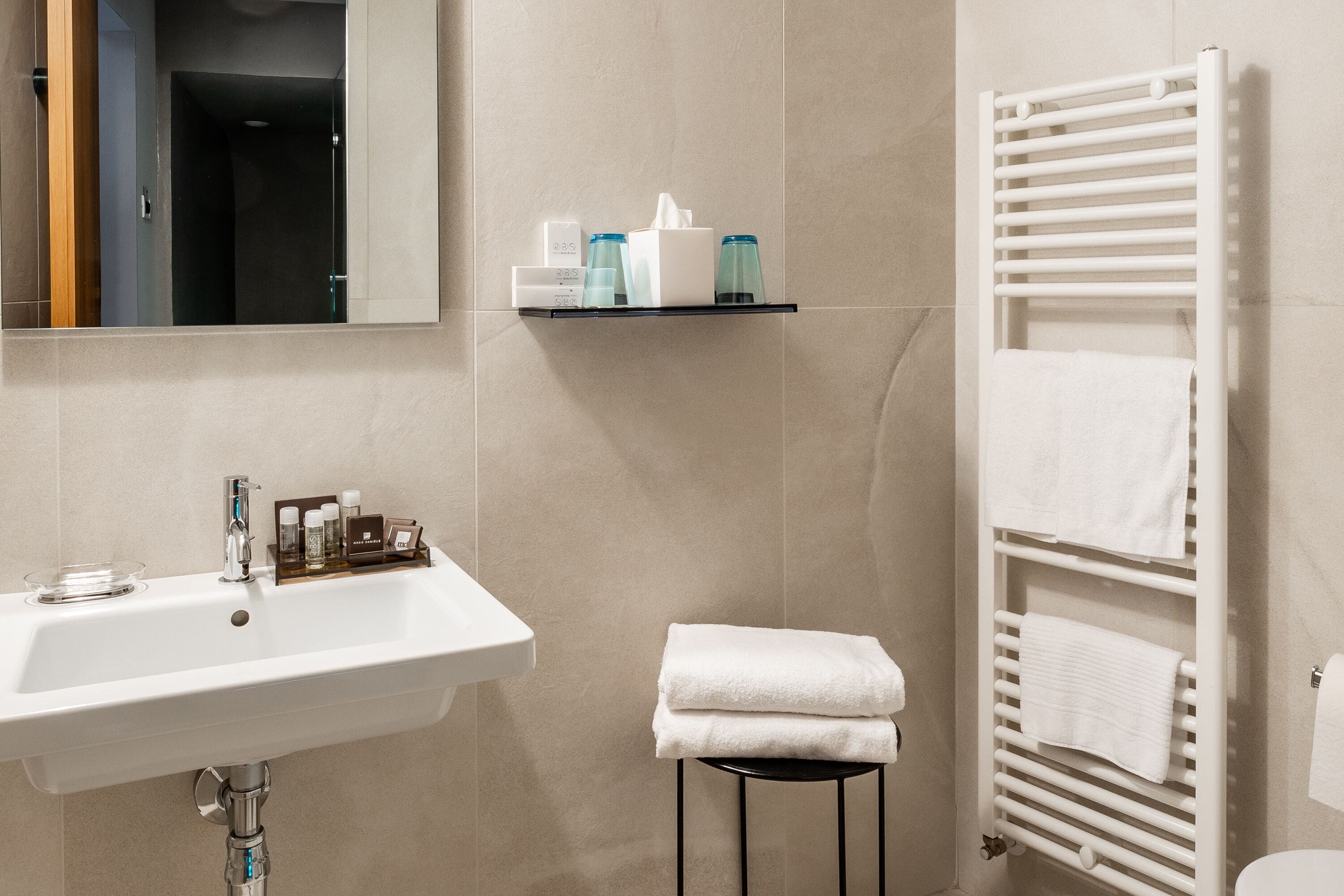 A modern bathroom with a white sink, a towel rack, and a shelf with toiletries.