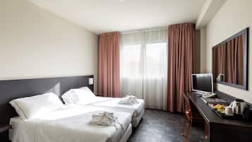 Une chambre d’hôtel avec deux lits, un bureau avec un ordinateur, un miroir et une fenêtre avec des rideaux.