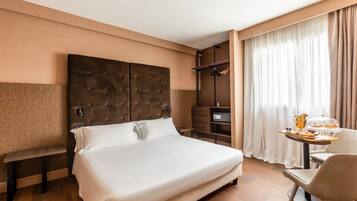 A hotel room with a large bed, a bench, a desk with a chair, a wardrobe, and a window with curtains.