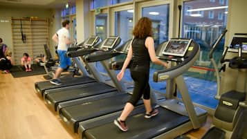 Et fitnessrum med løbebånd, trægulv og store vinduer.