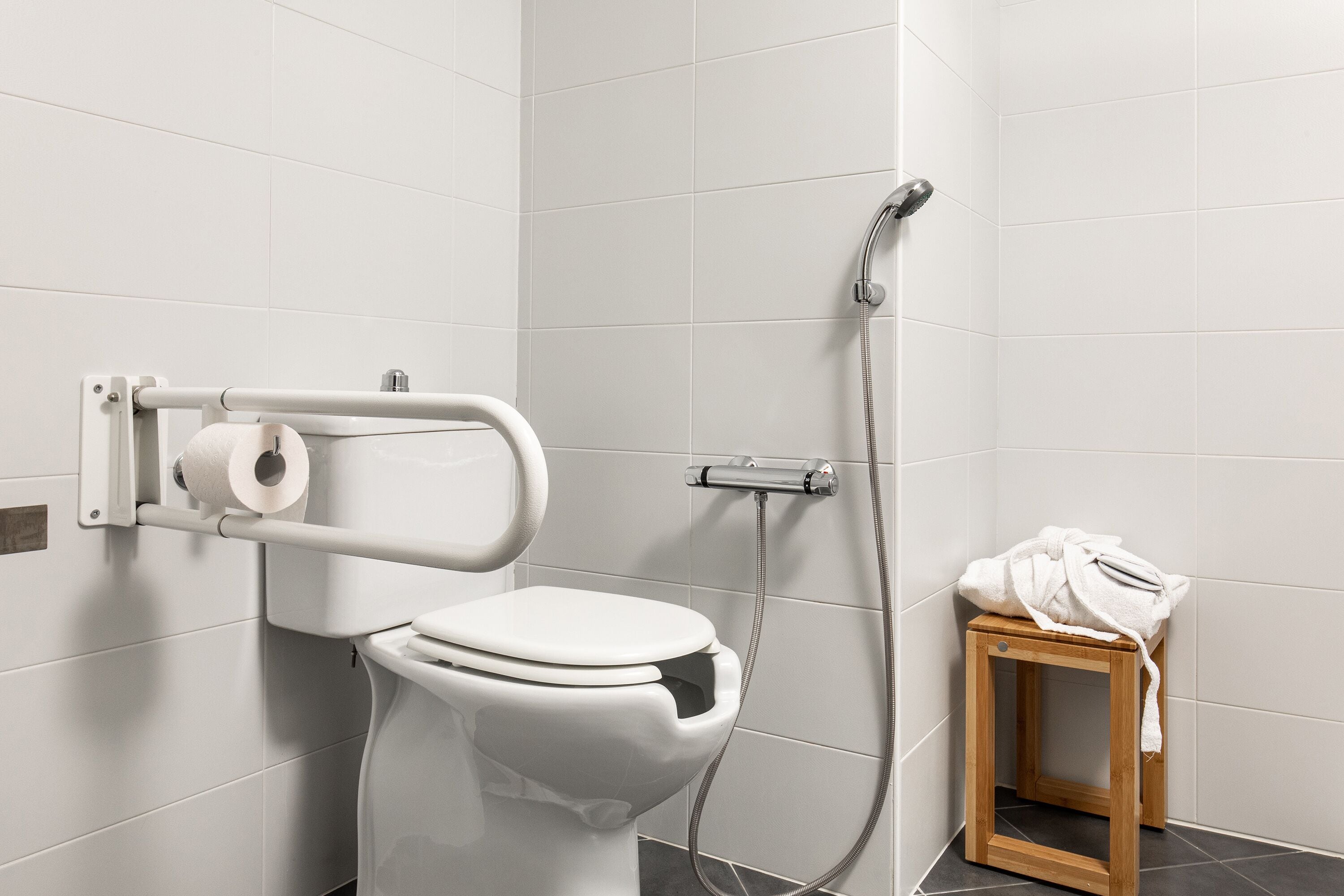 Een moderne badkamer met een toilet, een douche en een klein houten krukje.