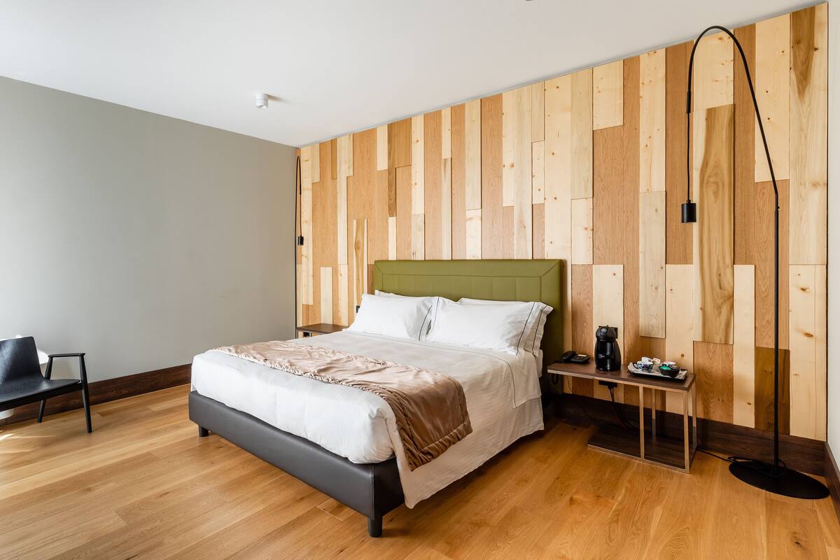 Ein modernes Schlafzimmer mit einer Holzwand, einem Bett mit weißer Bettwäsche, einem Nachttisch mit Lampe und einem Sessel.