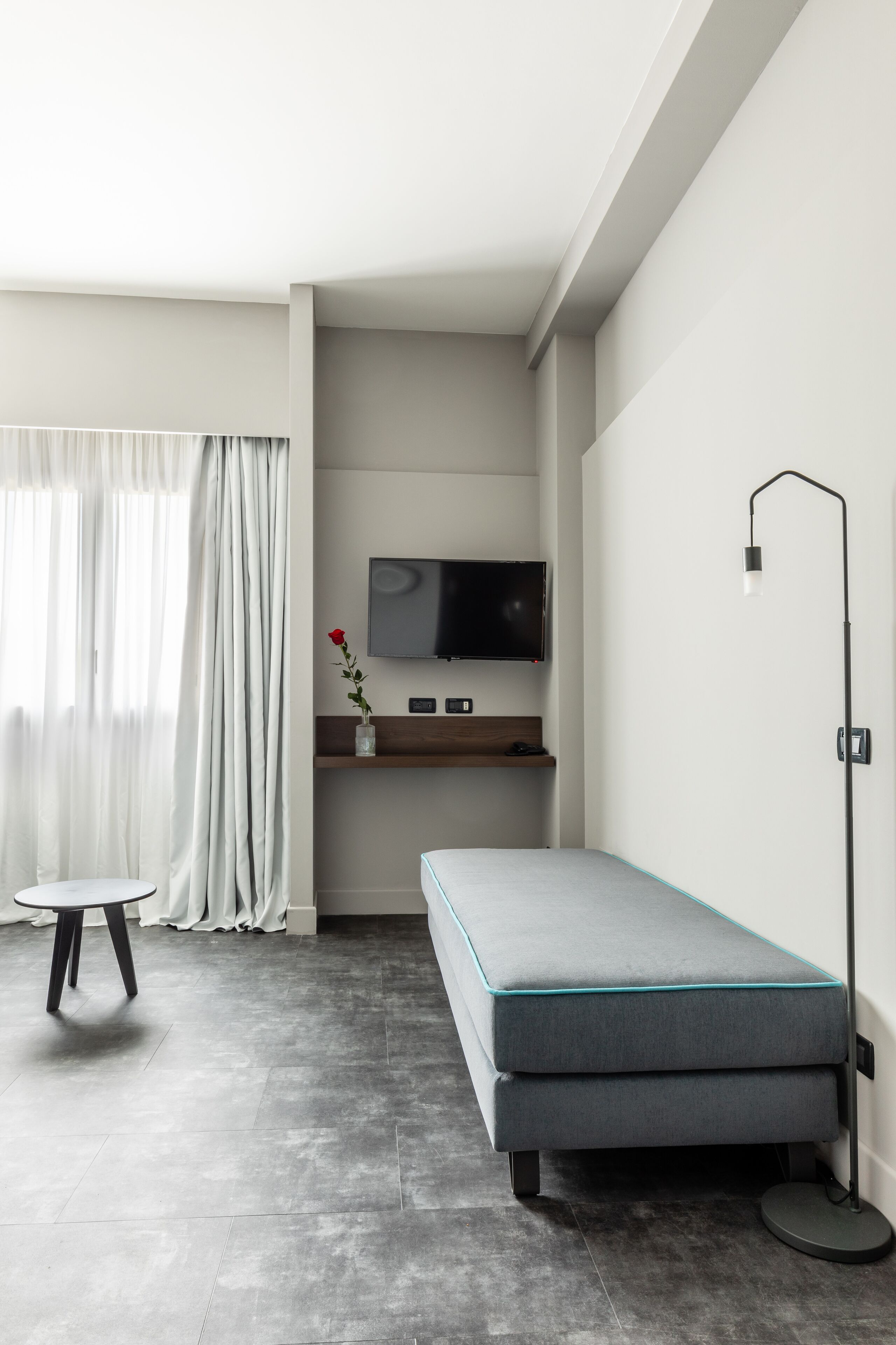 A modern room with a grey sofa, a small table, a TV mounted on the wall, and a floor lamp.