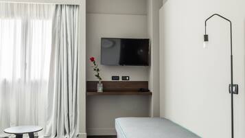 A modern room with a grey sofa, a small table, a TV mounted on the wall, and a floor lamp.
