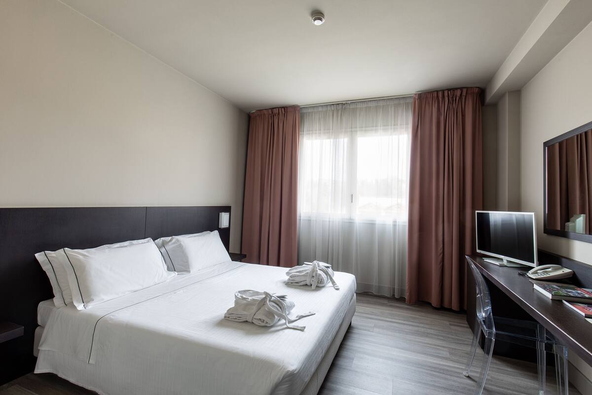 Ein Hotelzimmer mit einem großen Bett, einem Schreibtisch mit Computer und einem Fernseher.