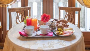 A breakfast table set with a floral tablecloth, two chairs, and a variety of breakfast items including eggs, pastries, and juice. - Dimora al Doge Beato Vista Canale (Venice)