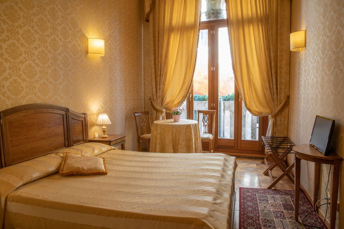 A hotel room with a large bed, a small round table, a chair, a desk with a computer, and curtains.