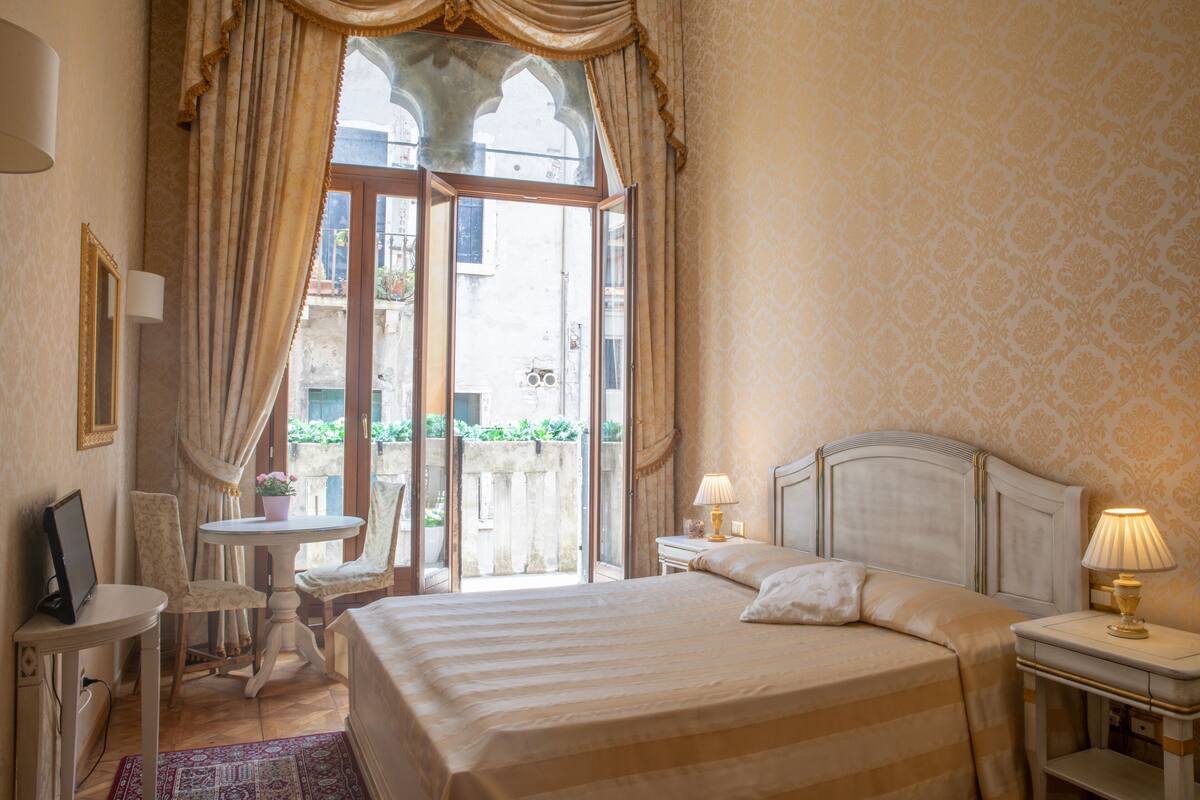 A hotel room with a bed, a small table, a chair, a desk, and a lamp.