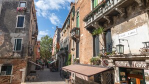 A narrow street with buildings on either side, outdoor seating, and a sign for 'Trattoria al Ponte'. - Dimora al Doge Beato Vista Canale (Venice)