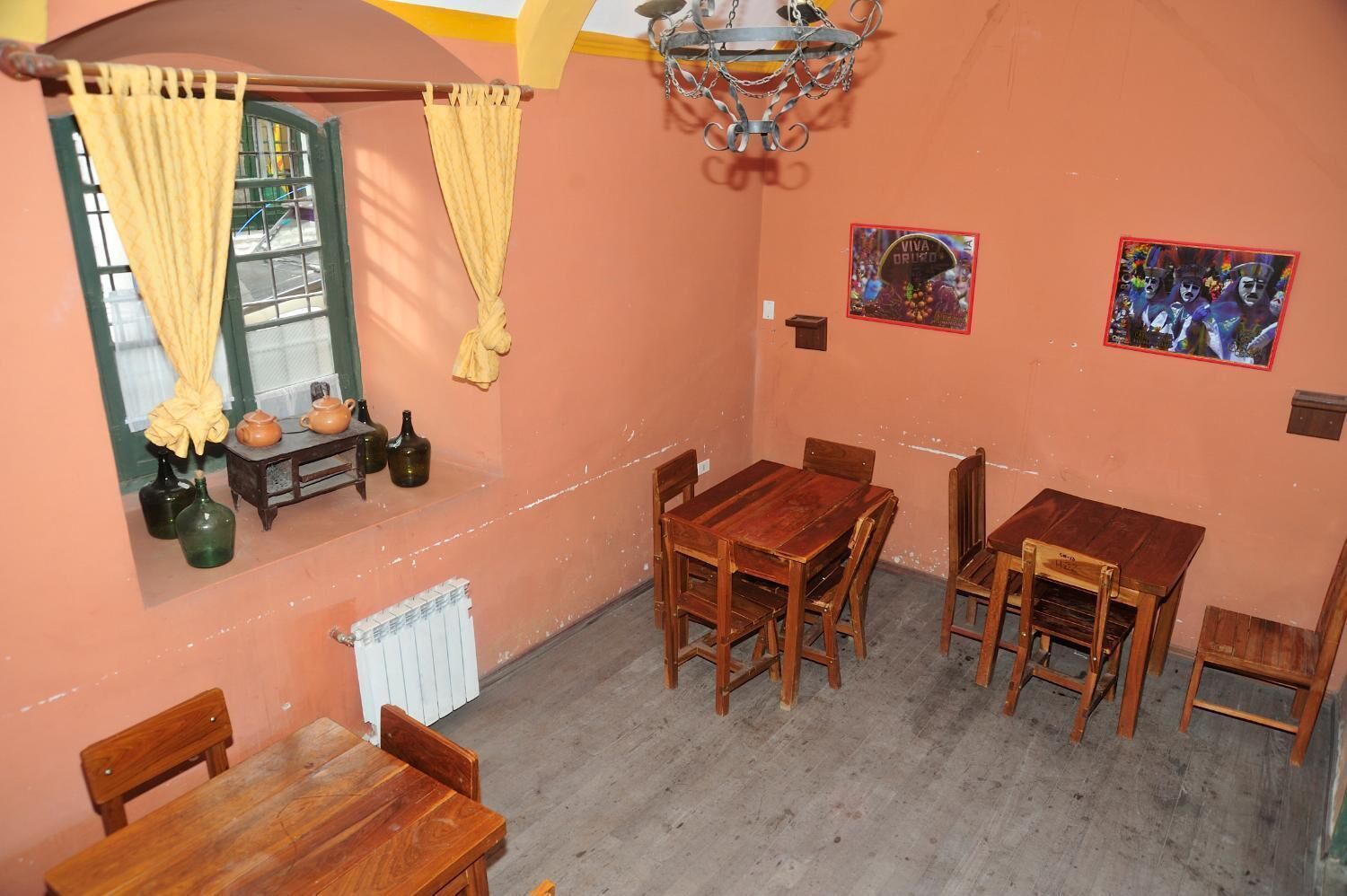 A dining area with wooden tables and chairs, a radiator, and a window with curtains.