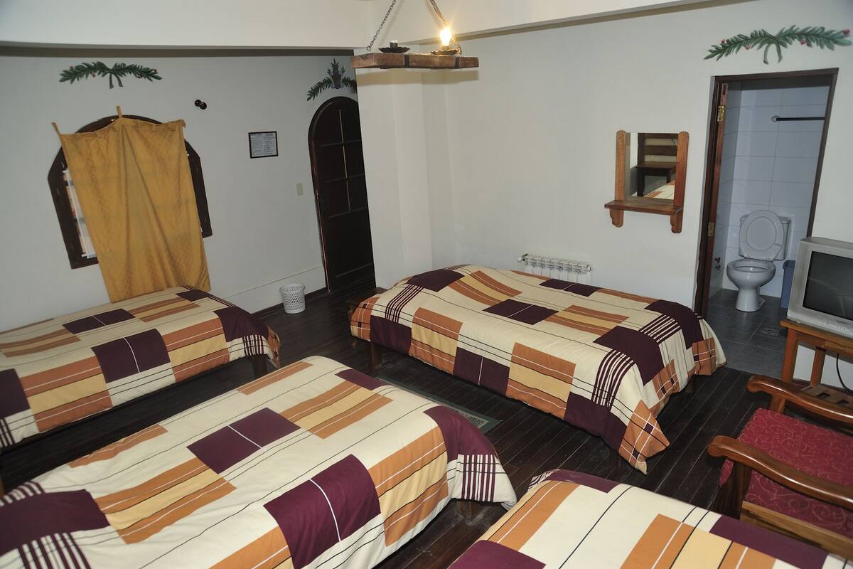 A room with three beds, a wooden chair, a television, and a door leading to a bathroom.
