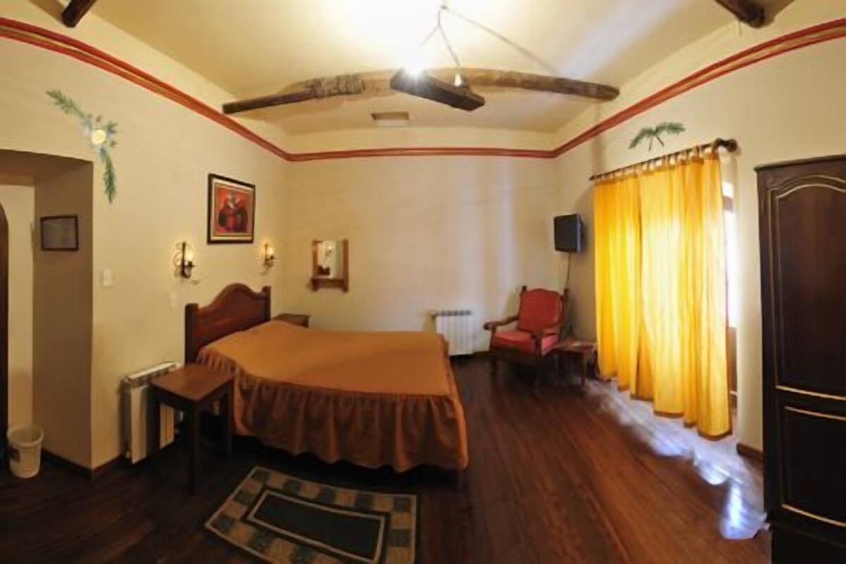 A hotel room with a large bed, a chair, a desk, and a radiator.