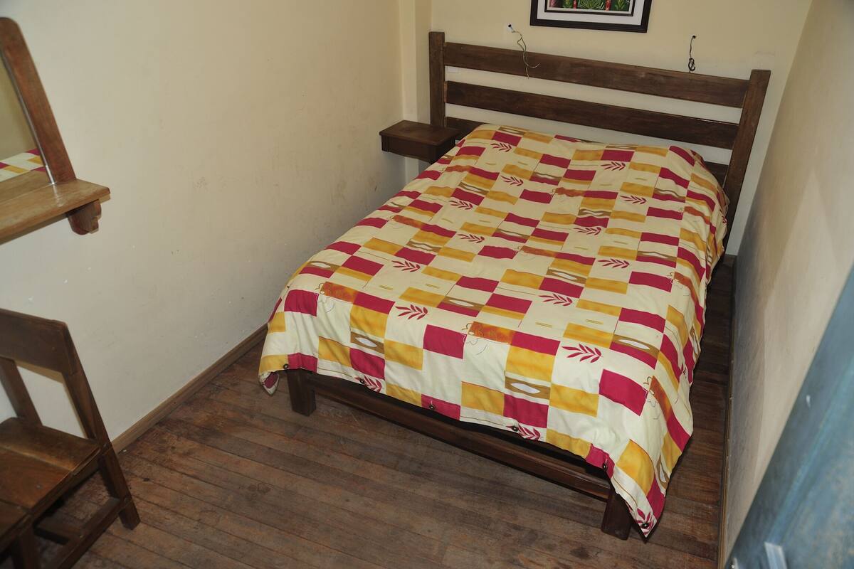 A small, single-bed room with a wooden headboard, a wooden nightstand, and a wooden chair.