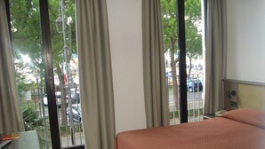 Une chambre d’hôtel avec un lit, un bureau et une vue sur la rue grâce à de grandes fenêtres.