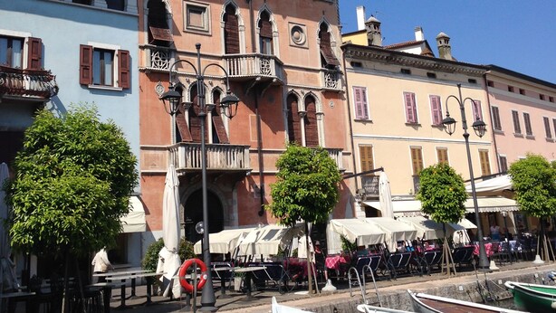 Un bâtiment situé au bord d’un canal, doté d’un balcon, avec une rangée de bateaux et un ciel bleu dégagé.