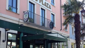 Un immeuble sur lequel on peut lire l’inscription « HÔTEL PLAZA », avec une voiture de sport rouge garée devant.