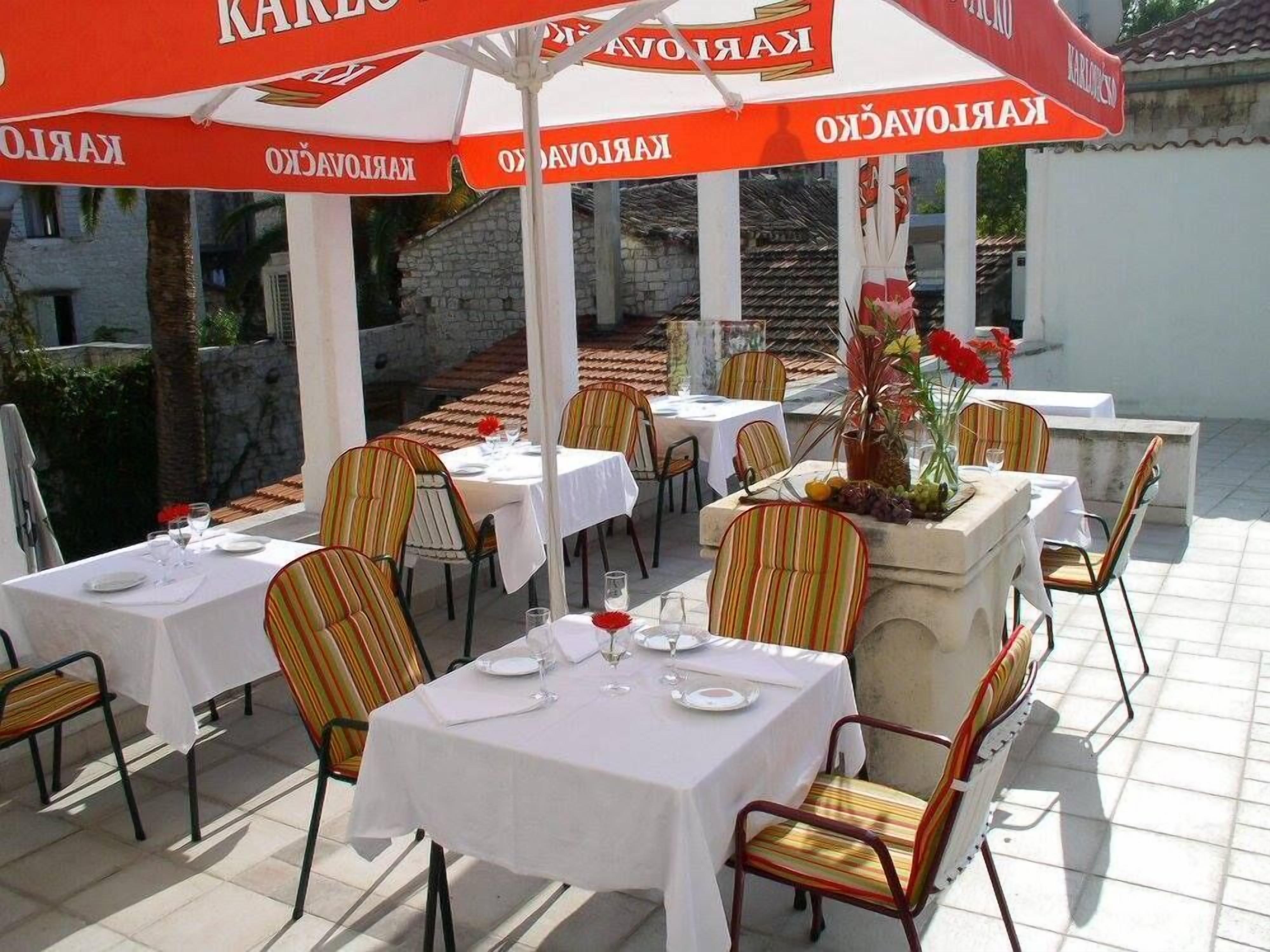 Un área de comedor al aire libre con mesas y sillas, cubierta por sombrillas con el nombre de marca 