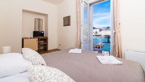 A hotel room with a bed, a TV, a desk, and a view of a pool and mountains. - Vila Liza (Trogir)