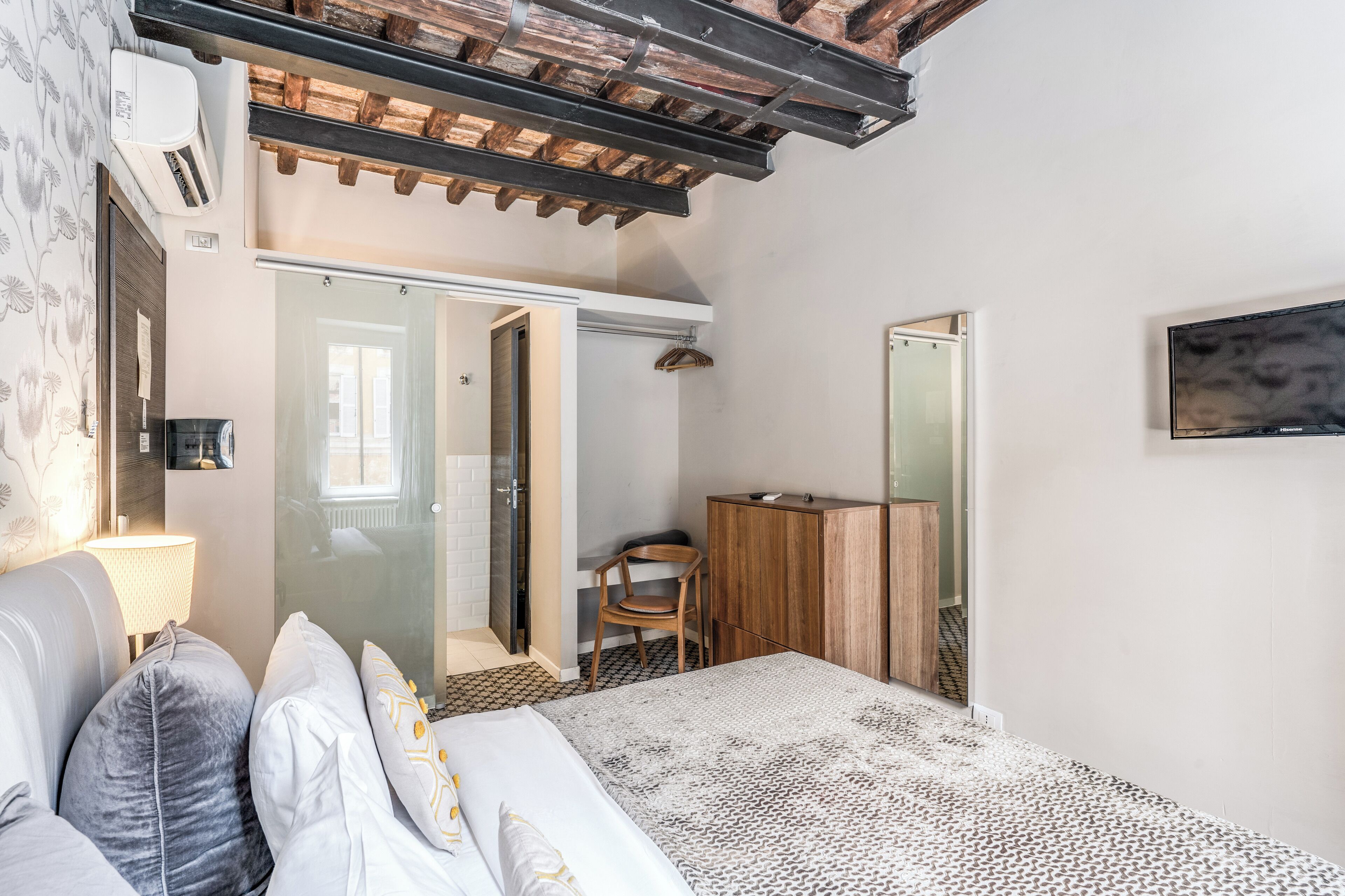 A bedroom with a bed, a wooden wardrobe, a chair, a desk, and a mirror.