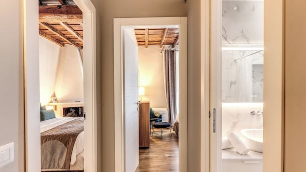 A narrow hallway leading to a bedroom with a bed, a wooden ceiling, and a bathroom with a bathtub and marble walls. - Trevi Beau Boutique Hotel (Rome)