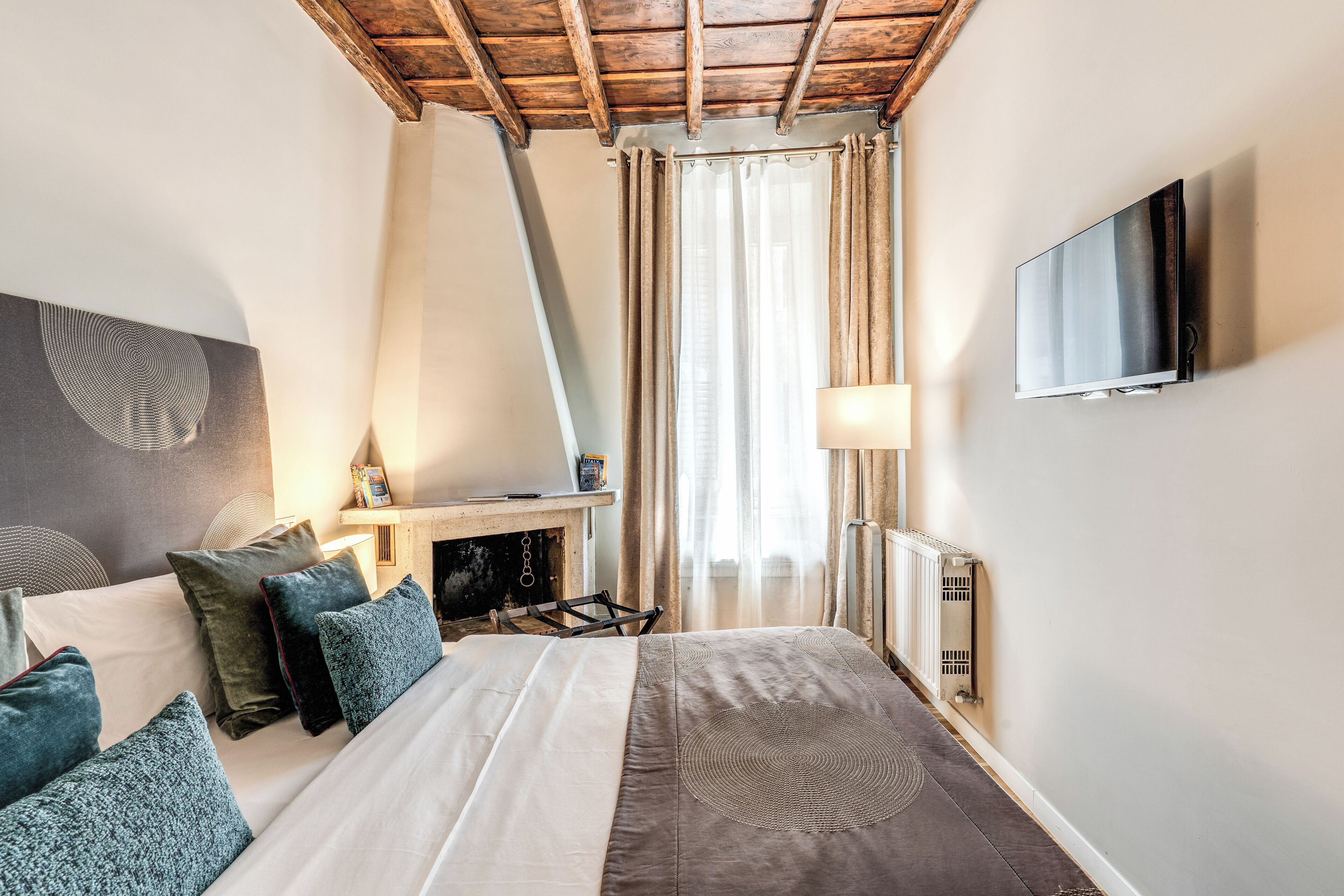 Habitación de hotel con cama, televisor montado en la pared, chimenea y ventana con cortinas.
