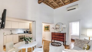 A modern kitchen with white cabinets, a dining table with chairs, a wooden ceiling, and a living area with a sofa and a lamp. - Trevi Beau Boutique Hotel (Rome)