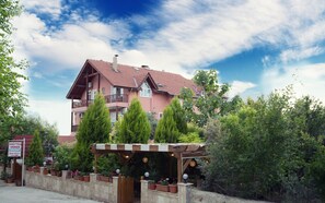 A pink multi-story hotel with balconies, surrounded by greenery and a wooden pergola. - Venus Hotel (Denizli)