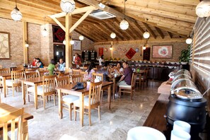 A restaurant with wooden tables and chairs, a buffet line, and a brick wall. - Venus Hotel (Denizli)
